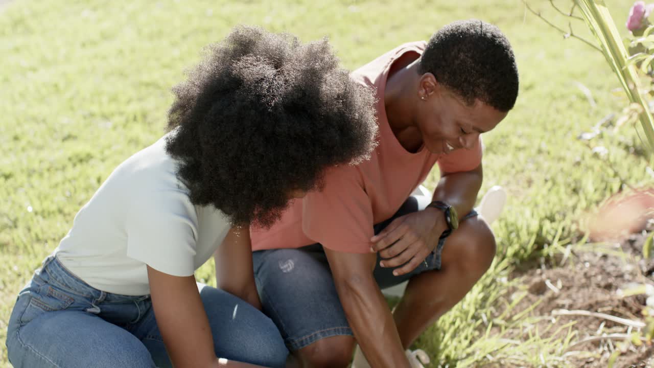 African American couple digging in yard removing plants from pots planting flowers for garden