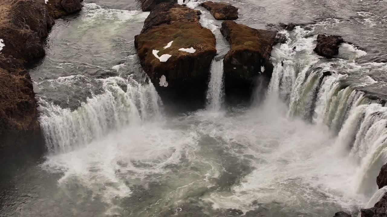 Aerial view of Goðafoss waterfall in Iceland, snow-covered rocks and water flow.