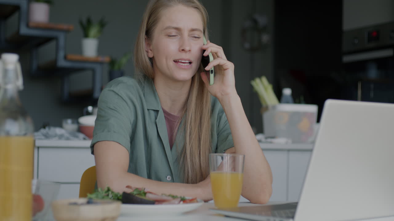 Kvinde arbejder hjemmefra, spiser morgenmad og taler i telefon.