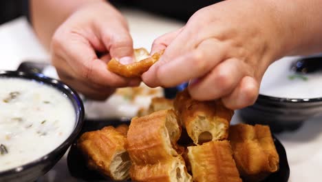 hands breaking dough sticks over a soup bowl