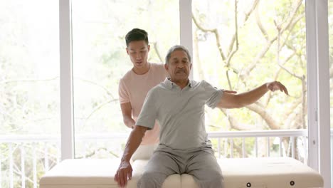 Diverse-male-physiotherapist-advising-and-senior-male-patient-stretching,-in-slow-motion