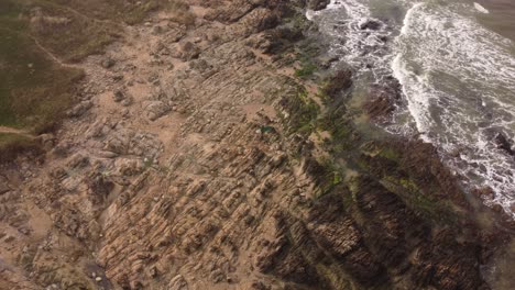 A-dynamic-orbital-aerial-footage-of-a-surfer-carrying-his-surfboard-while-walking-towards-the-water-by-the-seashore