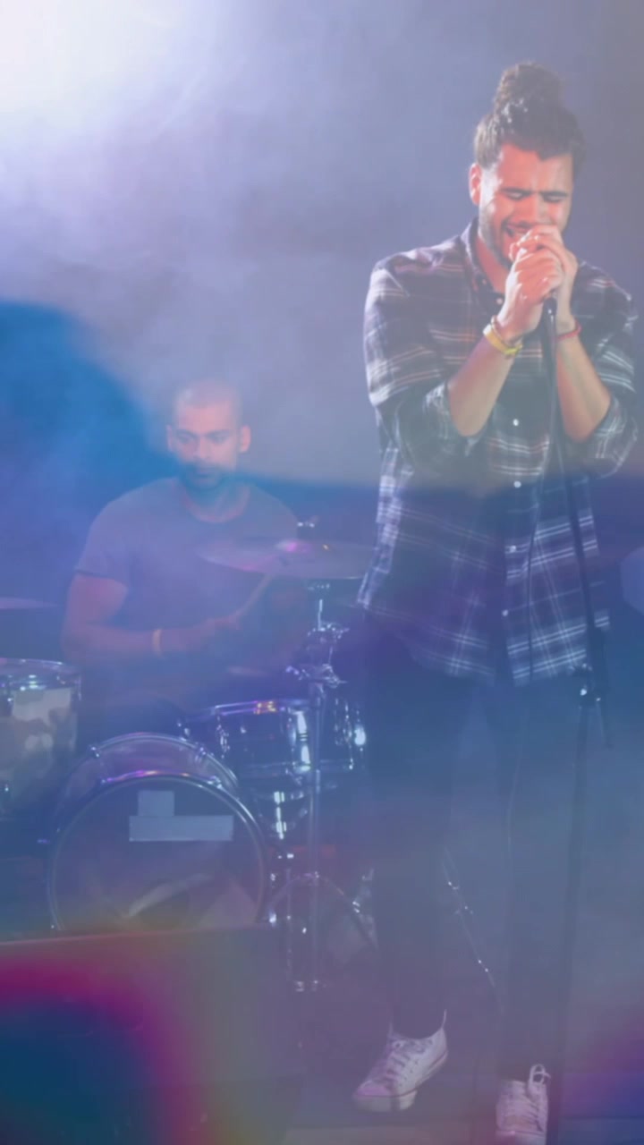 Animazione di luci blu incandescenti su un uomo caucasico che canta con una band che suona sul palco.