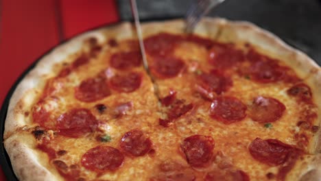 una pizza de pepperoni está cortada con un cuchillo, mostrando el queso y los ingredientes en una vista de cerca