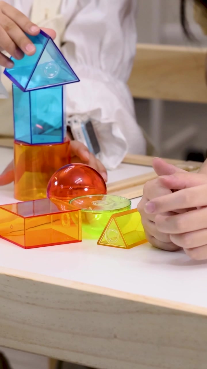 A child and adult collaborate to build a tower using bright, translucent geometric shapes.