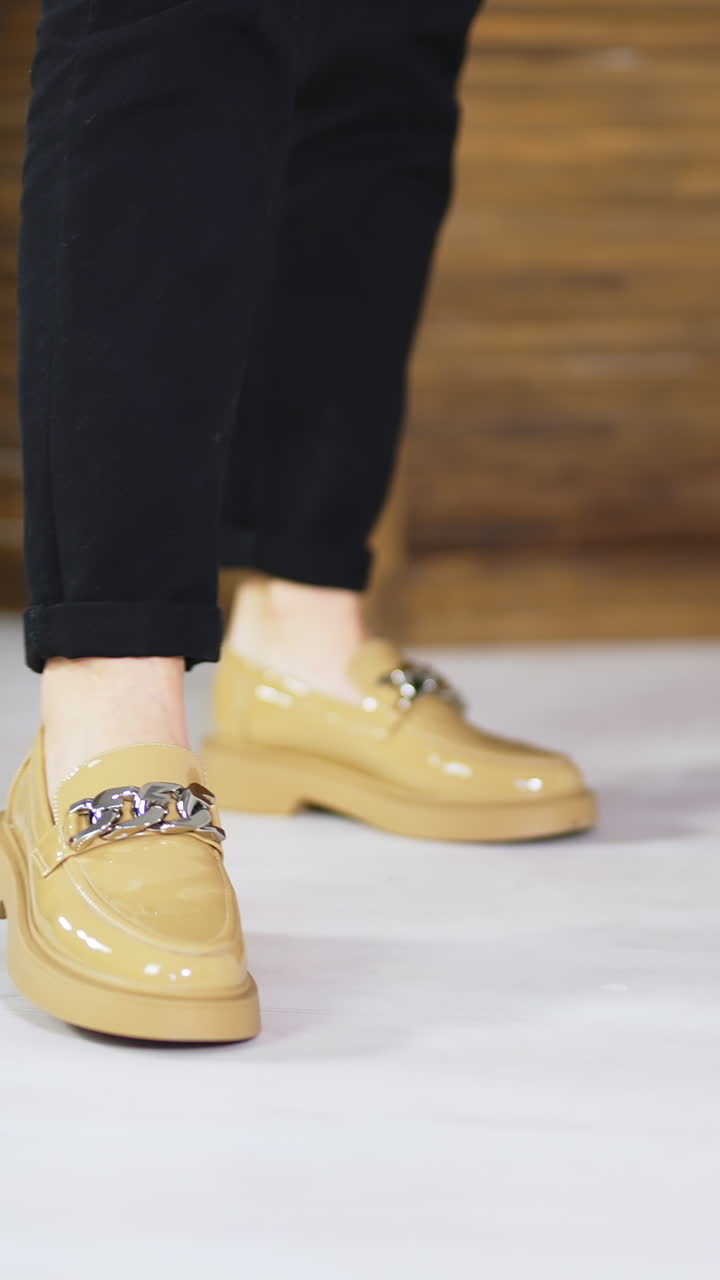Beige comfortable shoes on a female model wearing black jeans. Demonstrating new loafers with silver chain decoration. Vertical video