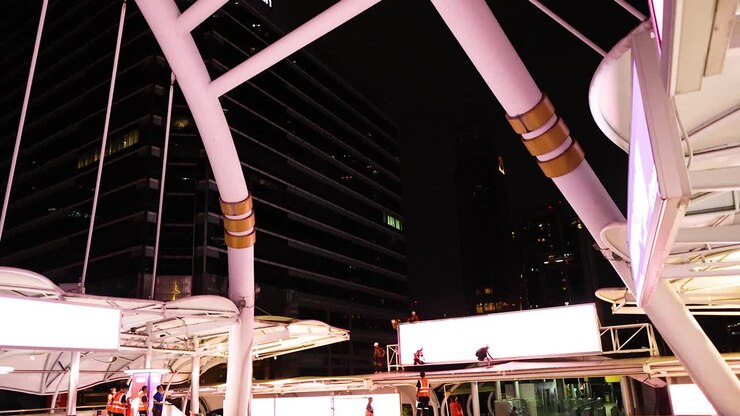 Camera tilts down Silom Bridge at night, revealing illuminated architecture and city life below