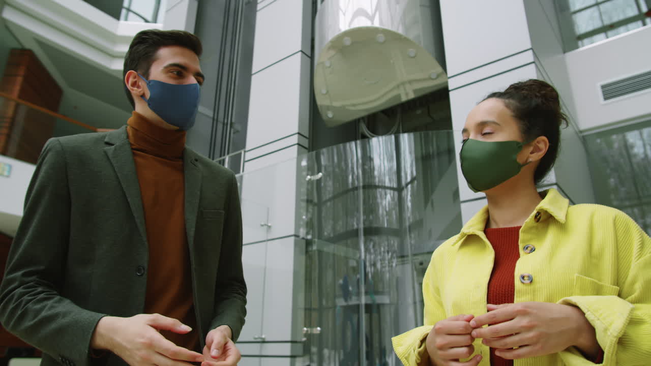 마스크를 입은 다양한 동료들이 사무실 센터에서 걸어다니며 이야기하고 있습니다.