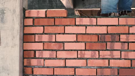 asian man laying bricks on top of mortar to build brick wall