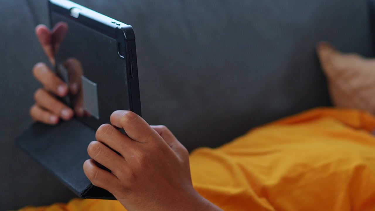 Close-up of hands using tablet screen while lying and relaxing on sofa