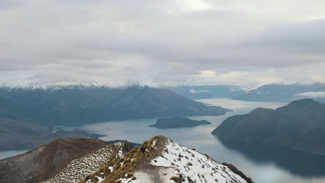 Hiker-walking-along-a-ridge-line-atop-of-Roys-Peak-in-Wanaka,-New-Zealand