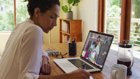 african american woman taking notes while having video call with male colleague on laptop at home