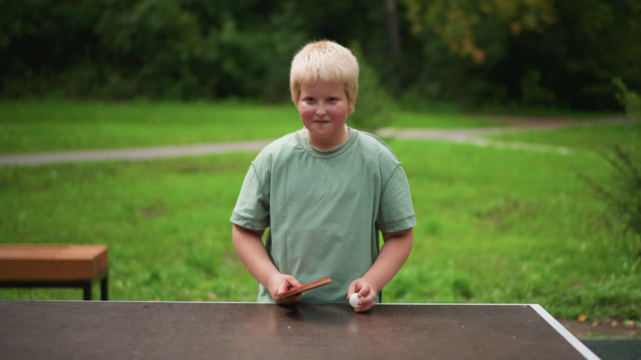 Focused Ping Pong Serve By Boy At Park Table, Steady Stance, Careful Grip, Ball Toss And Paddle Contact, Calm Concentrated Expression, Green Grass And Bench Backdrop, Practice Drills Improving