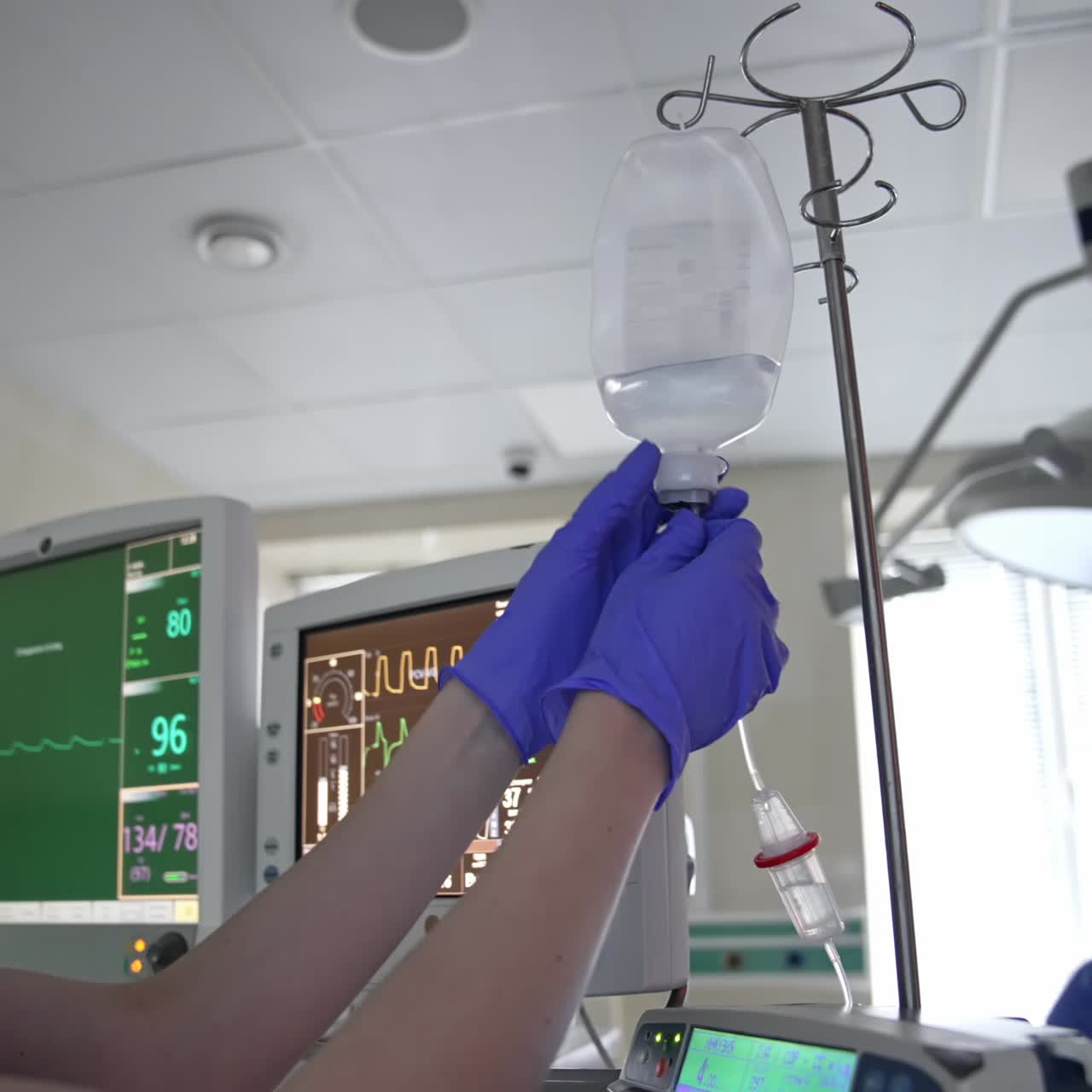 Anestesista donna che imposta il contagocce in sala operatoria. Un medico preme alcuni pulsanti sui monitor del ventilatore polmonare.