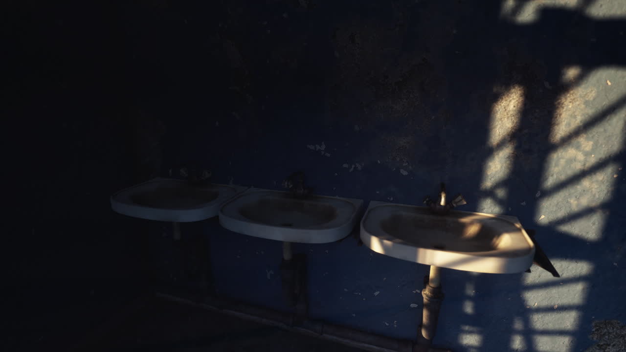 Abandoned restroom with three sinks and dark shadows on the wall