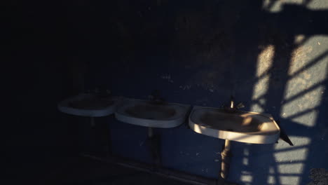 abandoned restroom with three sinks and dark shadows on the wall