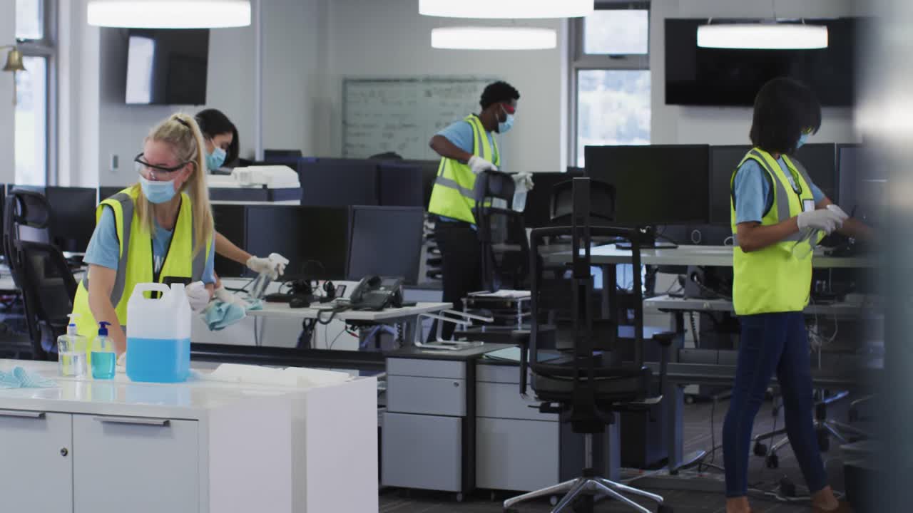 Equipe de colete de alta visibilidade e máscara facial limpando o escritório com desinfetante