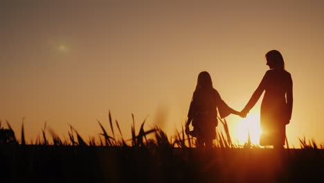 silhouettes in full growth of mother and daughter they stand in a picturesque place at sunset happy