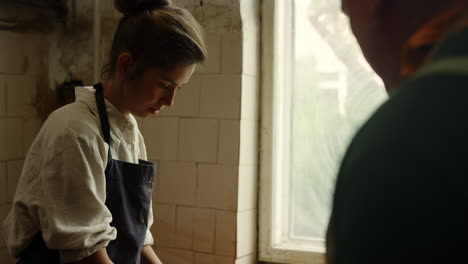 Man-giving-master-class-to-girl-in-pottery.-Lady-working-with-potters-wheel