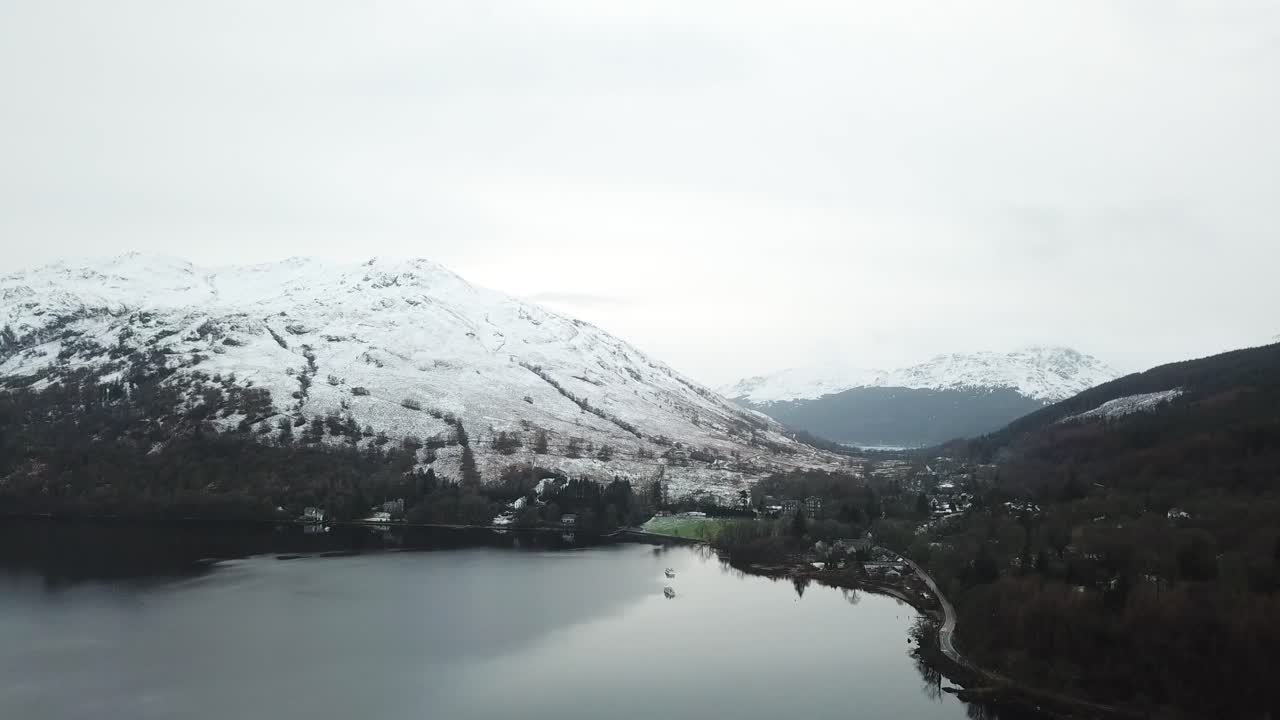 la nieve blanca cubrió las cimas de las montañas en el fondo con árboles en colores otoñales al lado de loch lomond en escocia