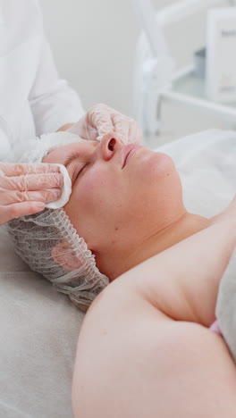 cosmetologist doctor wipes woman face and neck cleaning procedure with cotton pads in beauty clinic