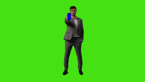 serious businessman holding blue screen mobile phone towards camera standing against green screen background 1