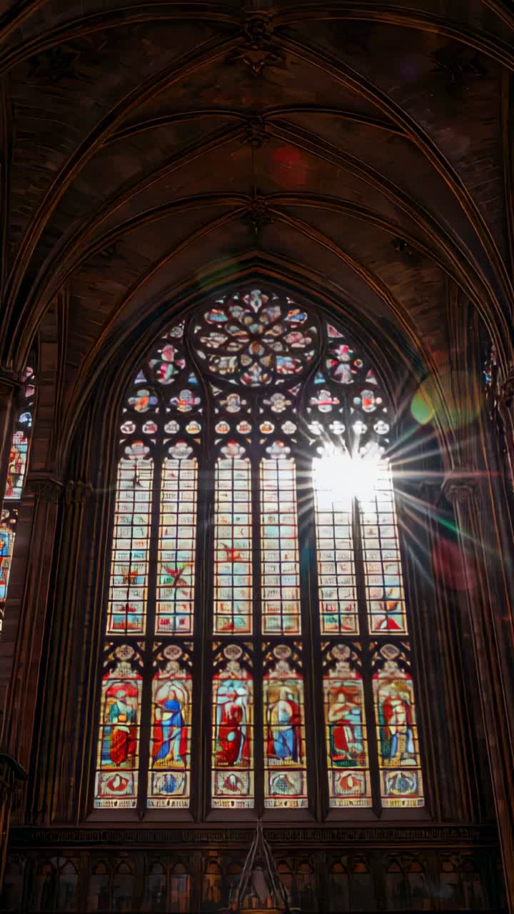 Vertical video: Showing Gothic window casting sunburst as sun aligns panes, lighting saints in nave