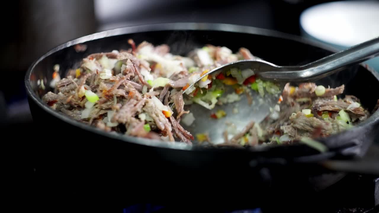 Close up slow motion view of a spoon stirring a beef stew with vegetables in a pan in a restaurant cuisine kitchen.