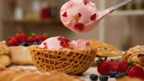 scooping strawberry ice cream into a waffle bowl