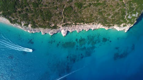 bird eye view drone shot of albanian coast in the mediterranean sea - drone is descending, watching a speed boat