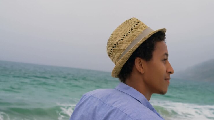 Side view of African American man in hat standing on the beach 4k