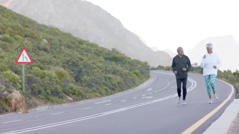 happy senior biracial couple running on road in mountains