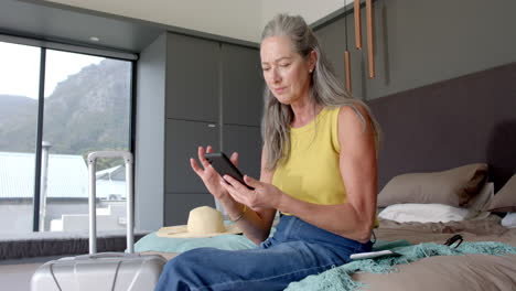 mature caucasian woman holding smartphone, sitting on bed