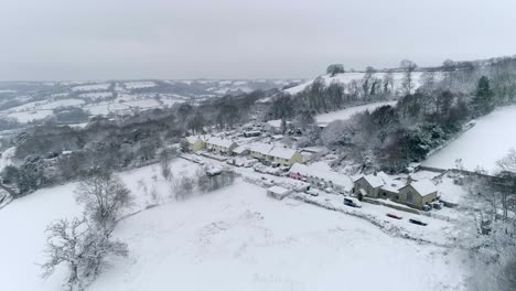 Seguimiento-Aéreo-Hacia-Un-Pintoresco-Pueblo-Inglés-Con-Coloridas-Casas-Y-Cabañas-Con-Techo-De-Paja,-Todas-Cubiertas-Por-Un-Manto-De-Nieve-Invernal.