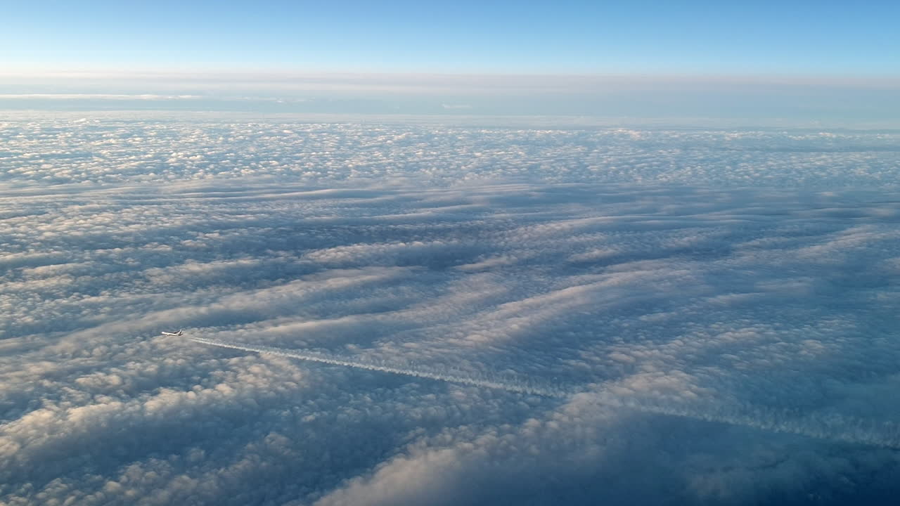 Incredible view from the cockpit of an airplane flying high above the clouds leaving a long white condensation vapour air trail in the blue sky
