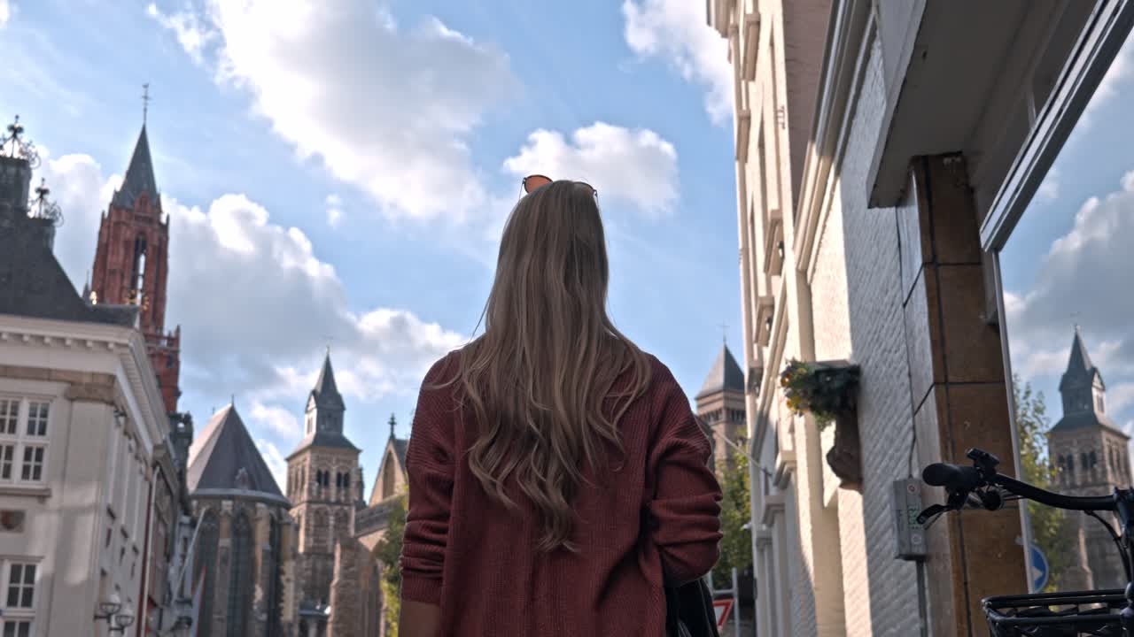 Woman in Vrijthof square on a sunny day, the historic center of Maastricht, Netherlands. The background is dominated by the iconic red tower of the Sint-Janskerk (St. John's Church)