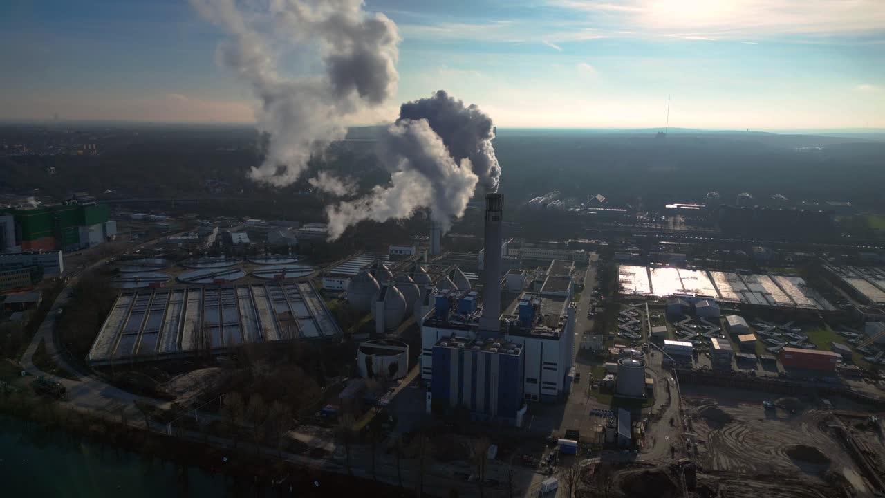 Industrial chimneys emitting white smoke over city skyline under blue sky, concept of pollution. Lovely aerial view flight static tripod hovering drone