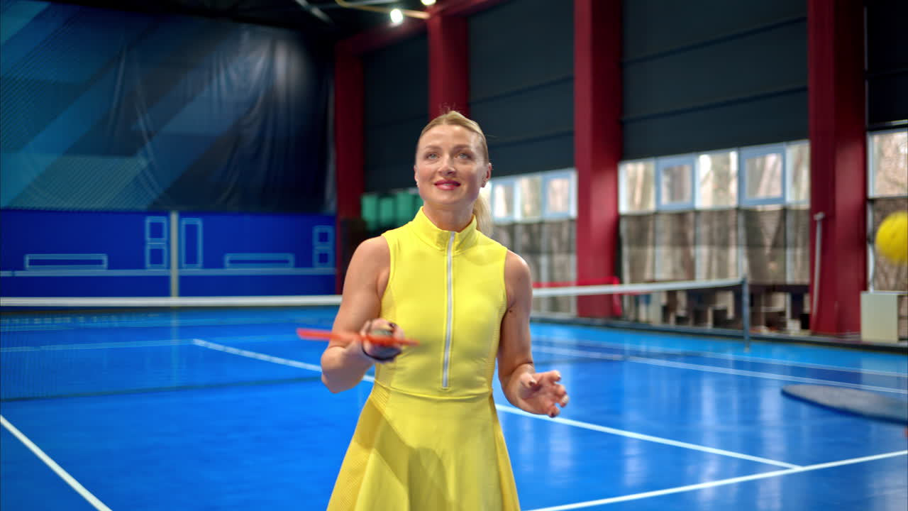 Woman in a yellow dress training to play pickleball on a blue, inside court
