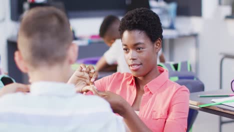 Vielfältige-Lehrerinnen-Und-Glückliche-Schulkinder-An-Schreibtischen,-Die-Im-Klassenzimmer-Gebärdensprache-Lernen