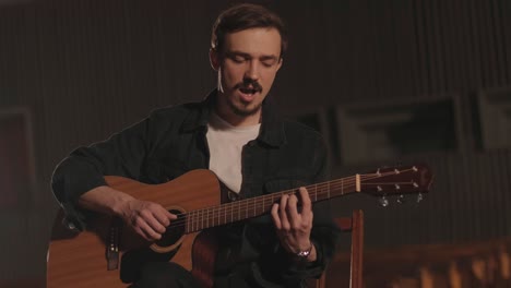 un chico guapo toca una guitarra acústica en un cine abandonado. el músico canta una canción y acompaña en la guitarra