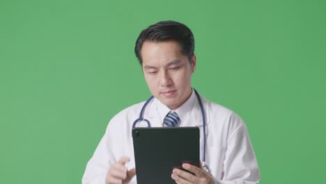 close up of asian male doctor with stethoscope using a tablet while walking on green screen background in the hospital