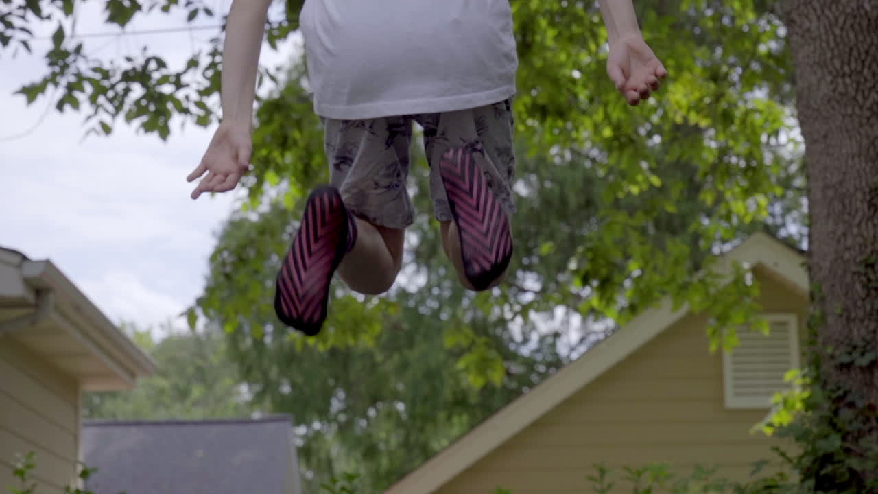 cute little boy jumping on trampoline, view from back side lifting feet in slow motion