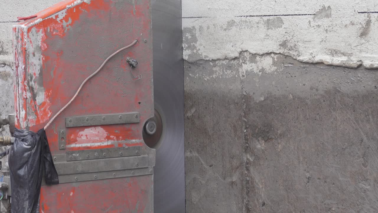 Close-up of a concrete wall saw with a large diamond-tipped blade, using water to cool and reduce dust while cutting through thick concrete or cement.