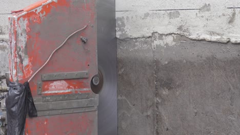close-up of a concrete wall saw with a large diamond-tipped blade, using water to cool and reduce dust while cutting through thick concrete or cement.