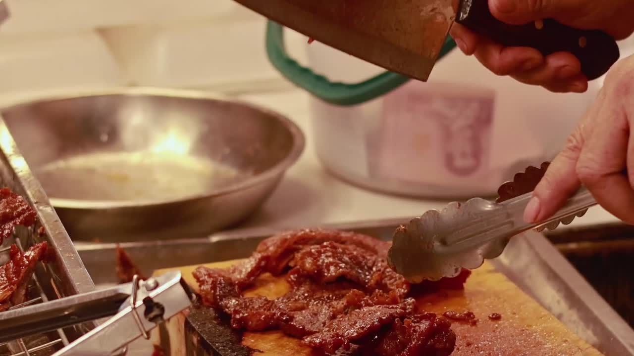 A detailed view of hands using a cleaver and tongs to chop meat on a cutting board.