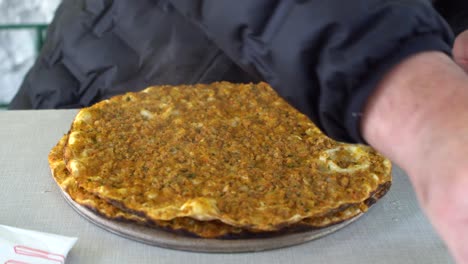 un hombre comiendo pizza tradicional turca (lahmacun) en un restaurante.