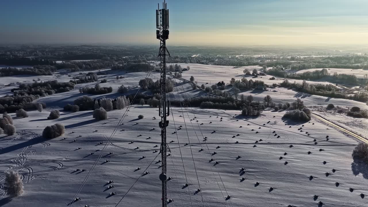 Vista aerea di un'antenna per cellulari in campi invernali sotto un sole splendente in un cielo blu.