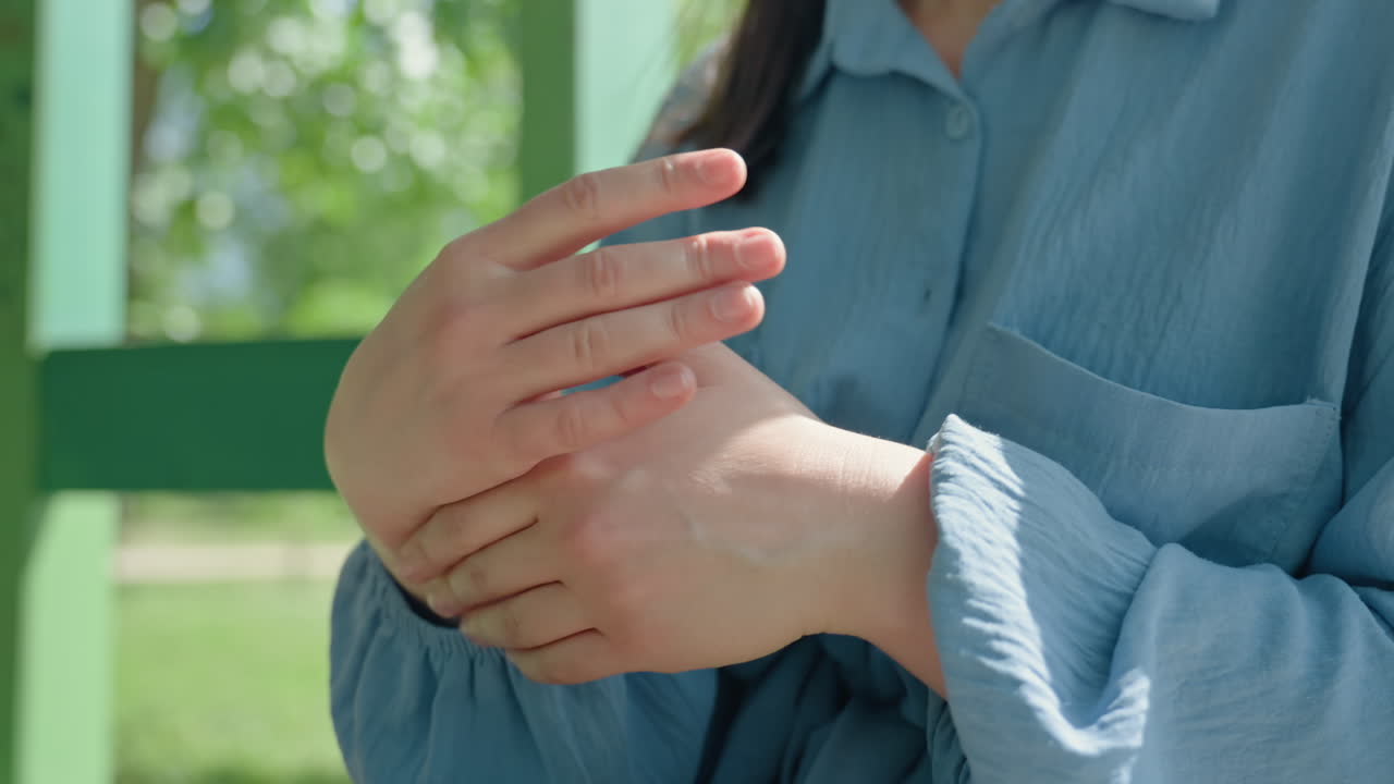 한 여성이 공원에서 차분하게 손 마사지를 제공하고, 평온한 여성이 자연 속에서 손 마사지로 자가 관리를 하며, 야외 공원에서 부드러운 마사지로 손을 진정시키는 여성의 평화로운 장면