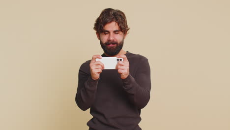 addicted man enthusiastically playing racing video games on mobile phone against beige background
