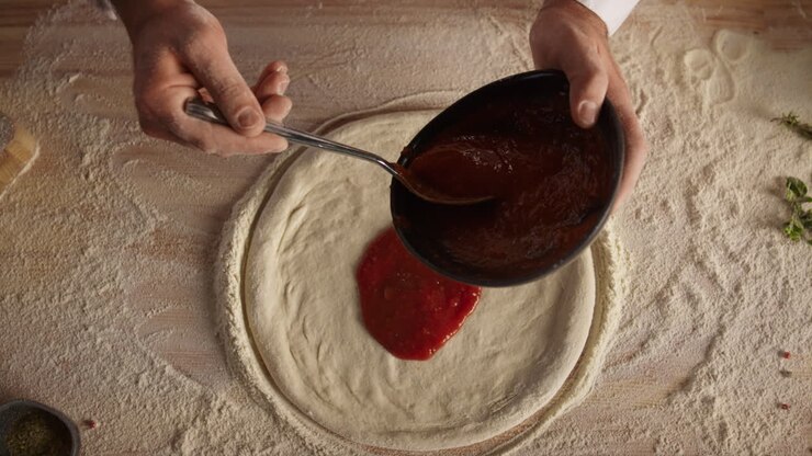 Chef spreading tomato sauce on pizza. Baker man hands cooking food in kitchen.